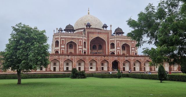 A domed red sandstone mausoleum seen across a green lawn with trees on either side.