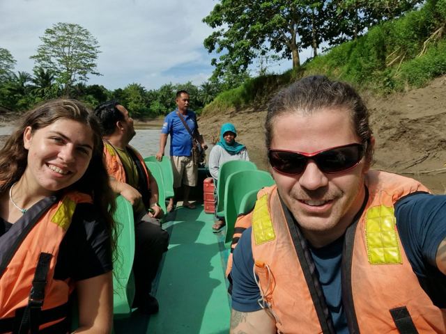 A man in sunglasses and a life jacket taking a selfie on a boat with other passengers.