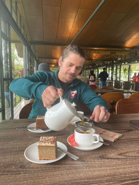 A man pouring tea from a teapot at a café table with cake.