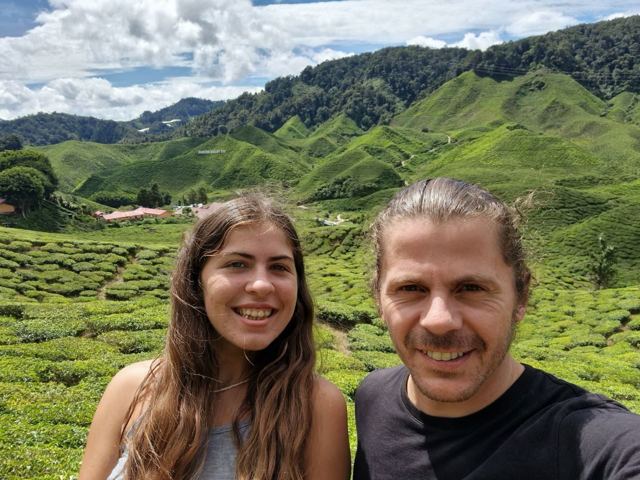 A man and a woman smiling in front of terraced tea plantations.