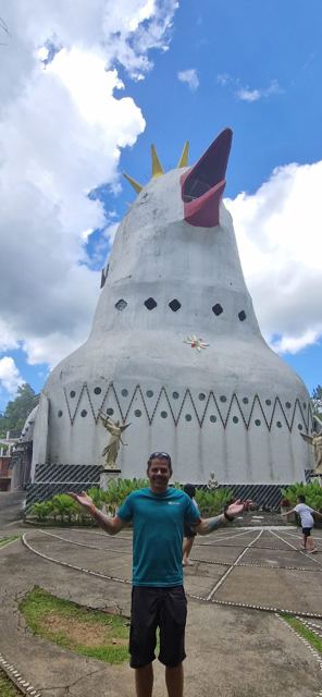 A man with arms out in front of a huge white church shaped like a bird.