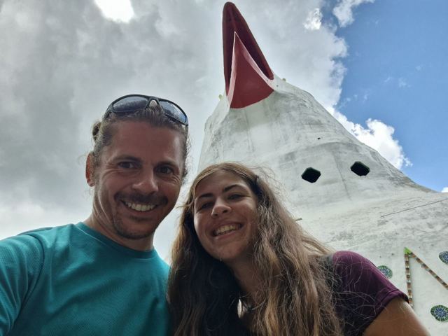 A man and a woman taking a selfie beside the giant bird-shaped Chicken Church.
