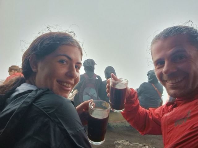 A man and a woman holding cups of coffee in the mist at a volcano summit.