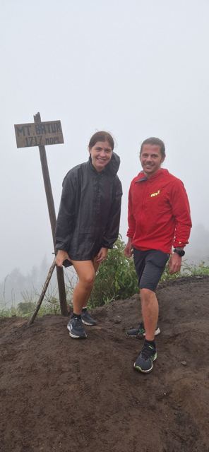 A man and a woman standing by the summit sign of Mount Batur in the mist.