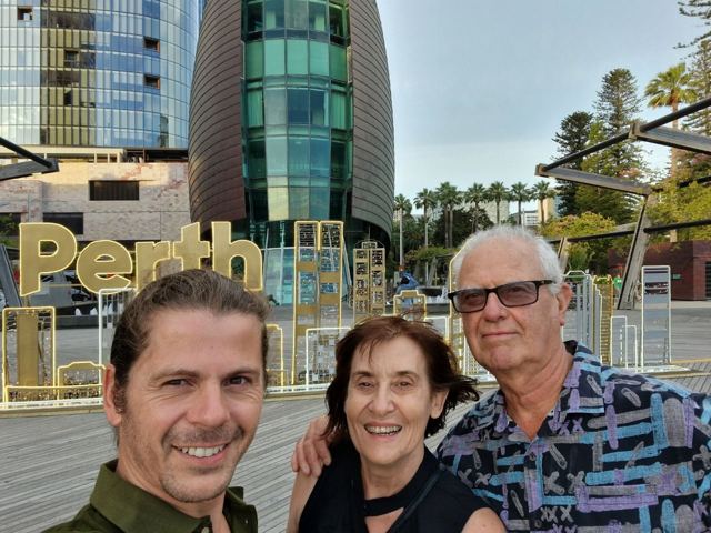 A smiling man taking a selfie with an older couple by the Perth sign on the waterfront.