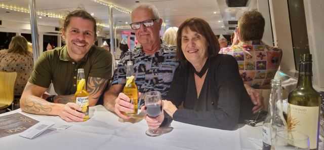 A man raising a beer at a restaurant table with an older couple.
