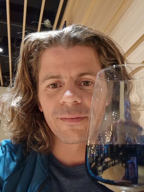 A man with long hair holding a wine glass in a terminal.