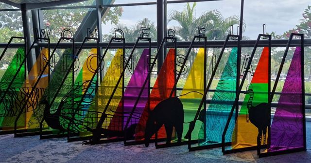 A row of tall, colourful stained-glass panels with tropical plants visible behind.