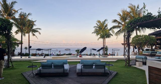 A resort lawn with two sun loungers, palm trees and the ocean beyond at dawn.