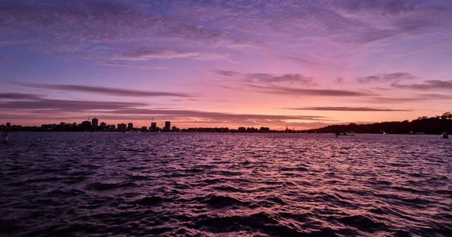A vivid purple and pink sunset over rippling river water with a distant city skyline.