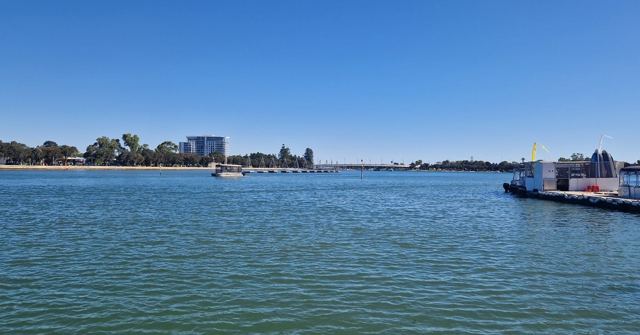 Calm blue estuary water under a clear sky with low buildings on the far shore.