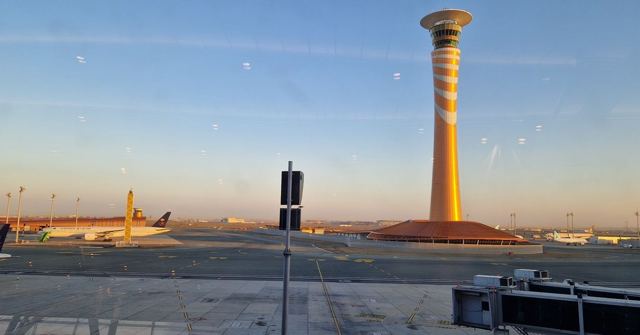 An orange and white airport control tower glowing in early evening light beside a runway.