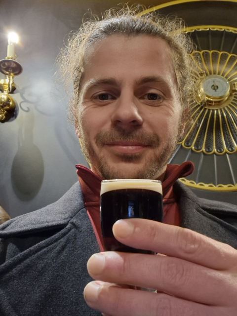 A man holding up a pint of Guinness in a pub.