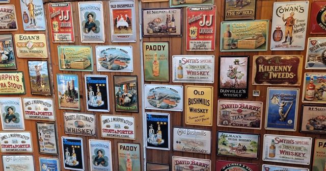 A wall covered in colourful vintage enamel signs advertising Irish whiskeys and other brands.