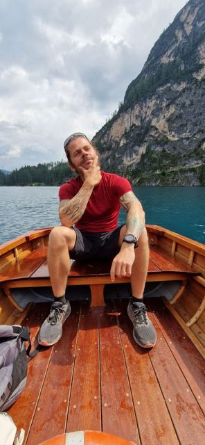 A man sitting in a wooden rowing boat on a turquoise mountain lake.