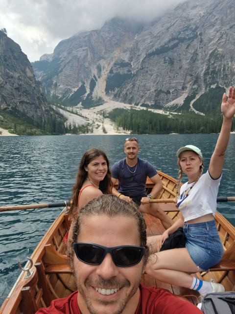 A group of friends in a wooden rowing boat on a lake surrounded by mountains.