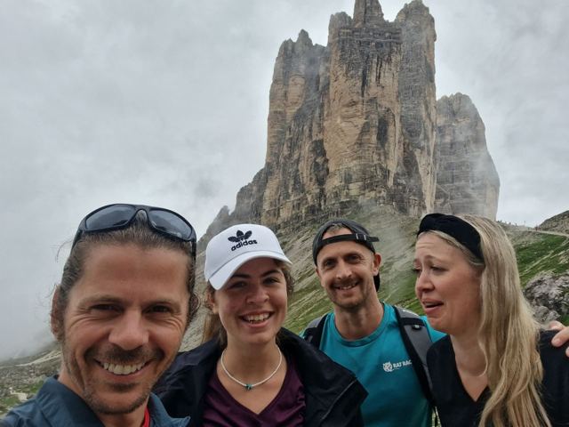 Friends smiling in front of the jagged peaks of the Tre Cime di Lavaredo.