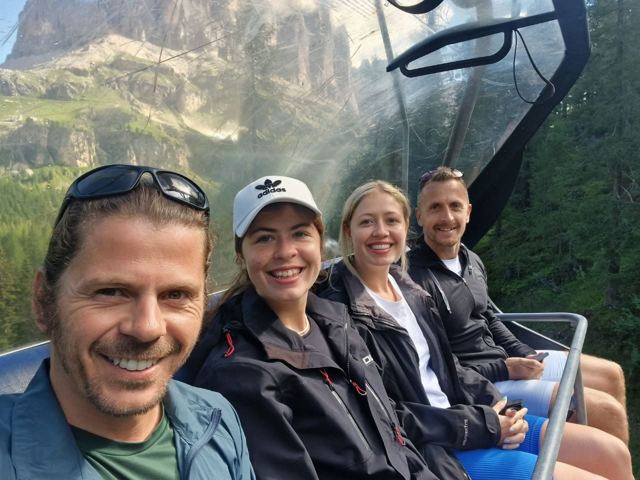 Friends smiling on a chairlift with Dolomite peaks behind.