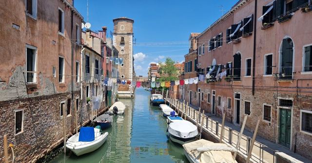 A narrow Venetian canal lined with old buildings, moored boats and laundry hanging out to dry.