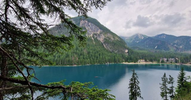 A turquoise alpine lake surrounded by pine forest and mountains, framed by overhanging branches.