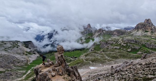 Rocky mountain peaks partly hidden by swirling clouds above a rugged green valley.