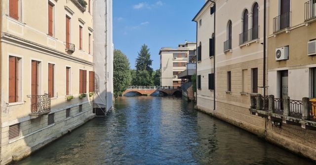 A calm canal lined with pale yellow buildings and a small bridge in the distance.