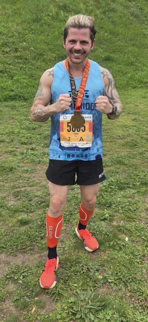 A man in a running vest and compression socks holding up his medal.