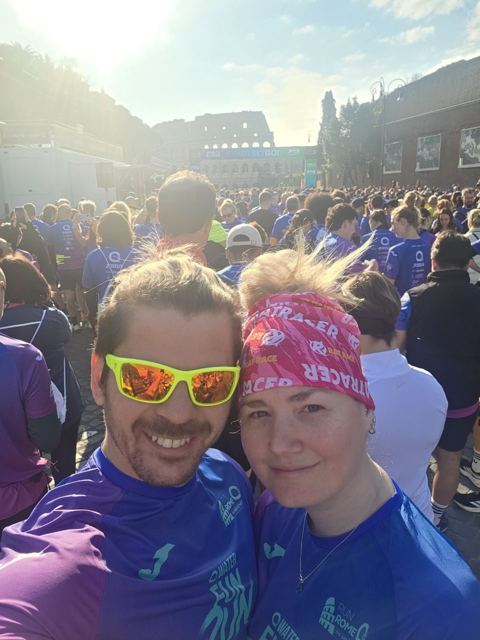 A man and a woman taking a selfie among runners near the Colosseum.