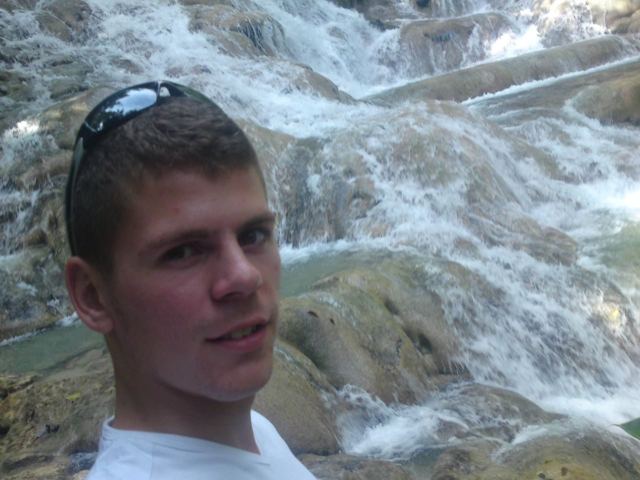 A smiling man with sunglasses on his head in front of cascading water at Dunn's River Falls.