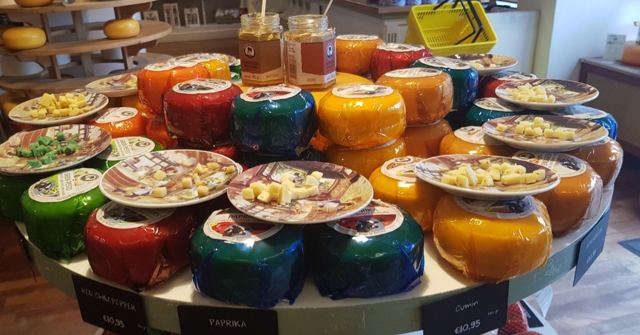 A round table of colourful wax-covered cheese wheels with tasting plates on top.