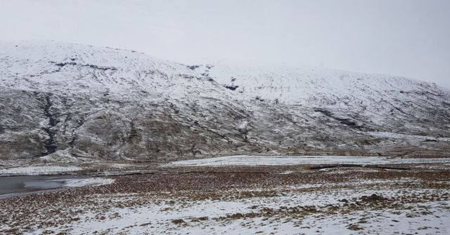 Snow-dusted brown hillsides above a flat snowy valley under grey sky.