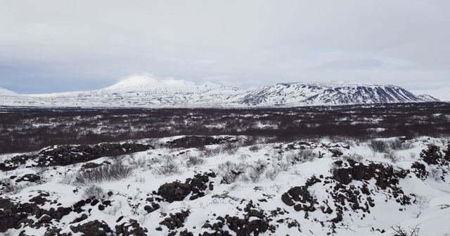 A snow-covered lava field stretching to distant snowy mountains.