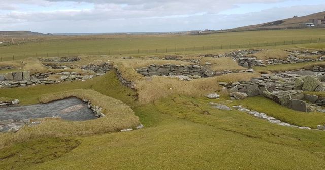 Grassy remains of ancient stone buildings on a green coastal headland.