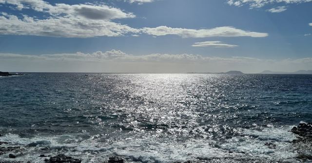Sunlight sparkling on a wide, choppy sea with a distant island under a blue sky.
