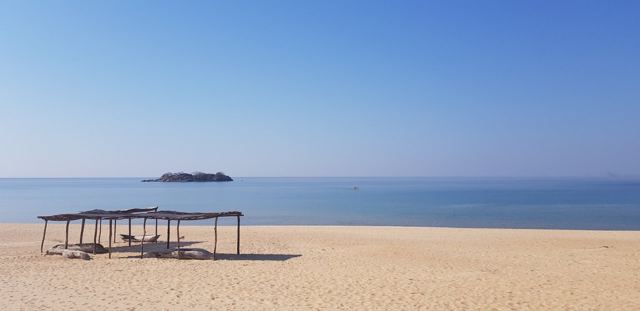 A thatched shelter on the beach and a small island out on Lake Malawi.