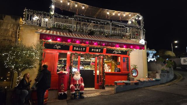 A red-fronted bar decorated with Christmas lights and a Santa figure at night in Valletta.