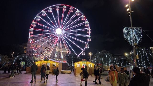 A brightly lit Ferris wheel at a Christmas market at night with festive light decorations.