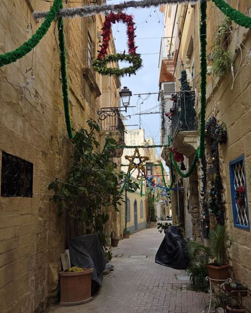 Narrow limestone alley decorated with Christmas bells, garlands and potted plants.