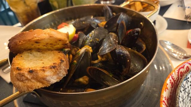 A metal pot of mussels topped with slices of toasted bread on a restaurant table.