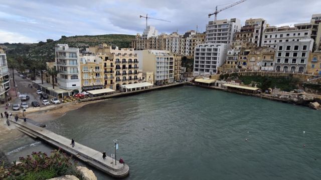 Narrow bay with green water and a stone jetty, surrounded by apartment buildings on a hillside.
