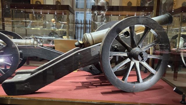Antique cannon on a wooden gun carriage displayed in a museum hall with glass cases behind.