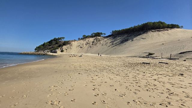 A huge sand dune sloping down to a beach and the sea under a clear blue sky.