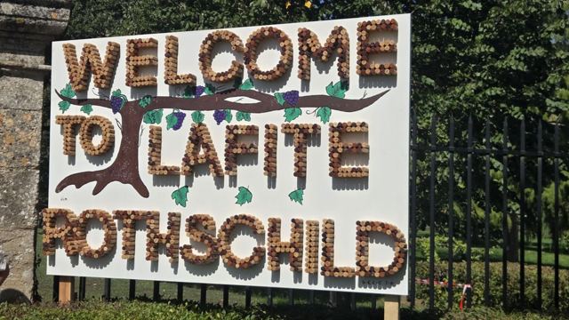 A sign spelling Welcome to Lafite Rothschild in wine corks, mounted on a fence.