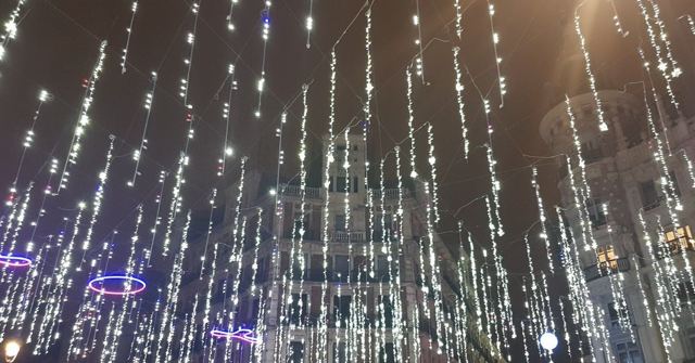 Hundreds of strings of white Christmas lights hanging down against a night sky.