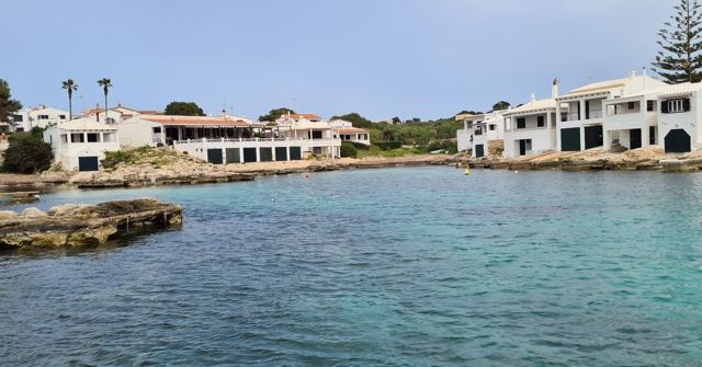 A clear turquoise inlet bordered by whitewashed houses and a few palm trees.
