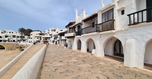 A stone path beside whitewashed houses with arched porches and wooden balconies.