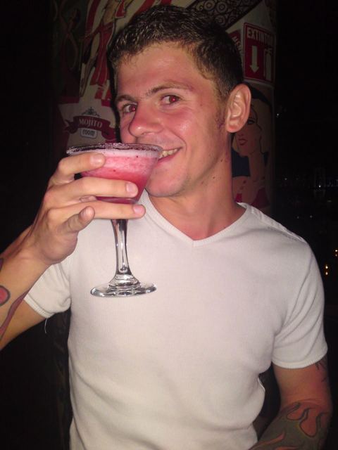 A man sipping a large pink frozen margarita in a bar.