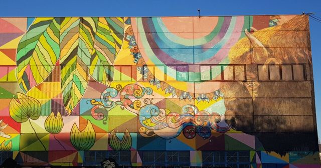 A large colourful geometric mural of leaves and patterns painted across a building facade.