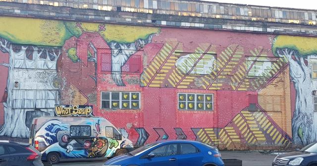 A building covered in a large colourful mural with a painted van parked in front.