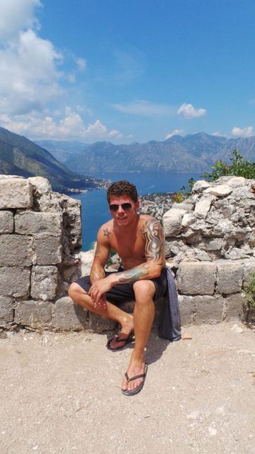 A man sitting on old stone walls high above the Bay of Kotor and its mountains.
